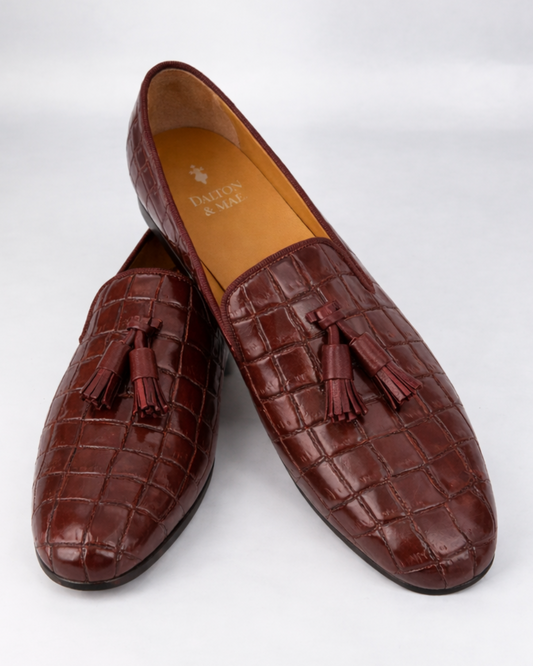 Pair of burgundy croc leather loafers with tassels on a white background